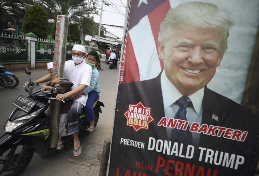A man and his sons wearing face masks ride past an advertisement using a portrait of US president Donald Trump in Indonesia (AP)