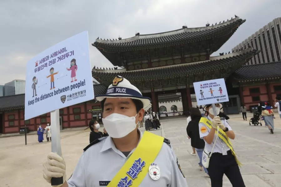South Korean tourist police officers wearing face masks hold up social distancing signs at the Gyeongbok Palace in Seoul, South Korea (Ahn Young-joon/AP)