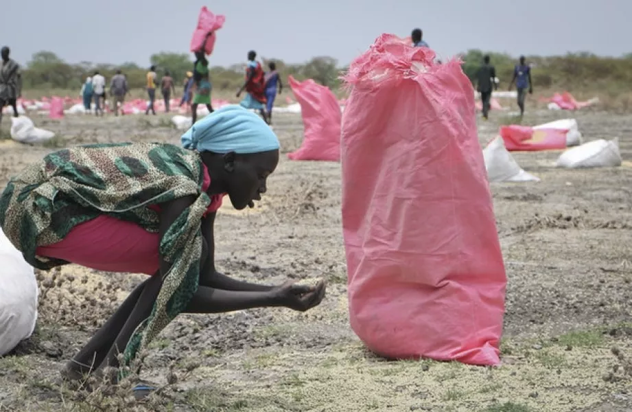 A woman scoops up fallen grain after an aerial food drop in Kandak, South Sudan (Sam Mednick/AP)