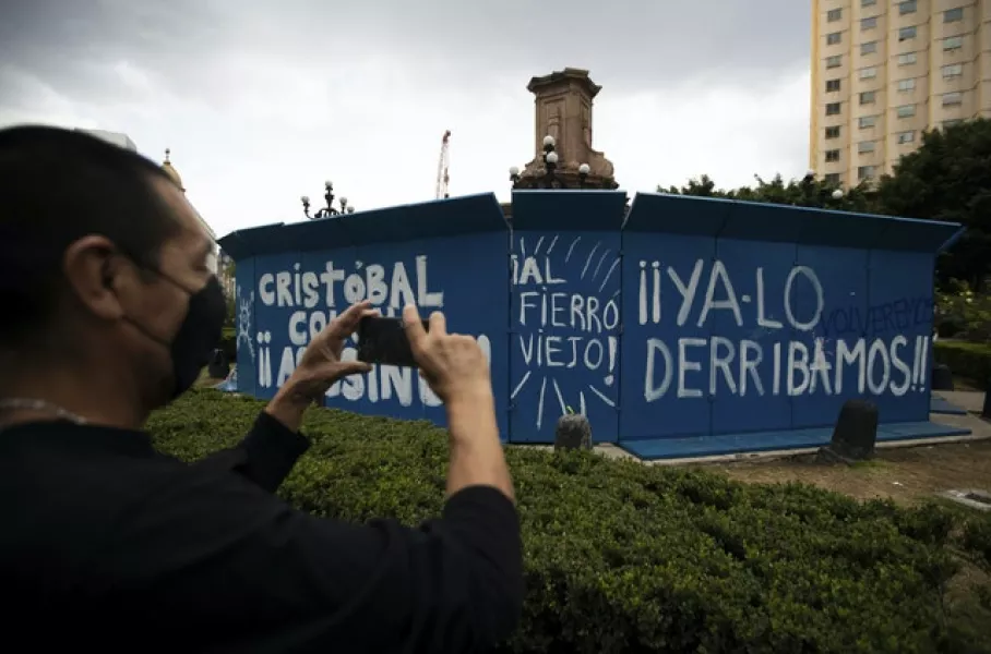 In Mexico City, a man takes a photo of graffiti that reads in Spanish “Christopher Columbus assassin, we’ve already knocked him down,” on a temporary metal barrier set up to protect the perimeter of the Christopher Columbus statue which was removed by authorities (Fernando Llano/AP)