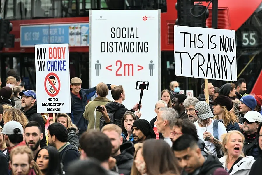 Protesters during an anti-lockdown rally pass a social distancing sign on Tottenham Court Road, London (Dominic Lipinski/PA)