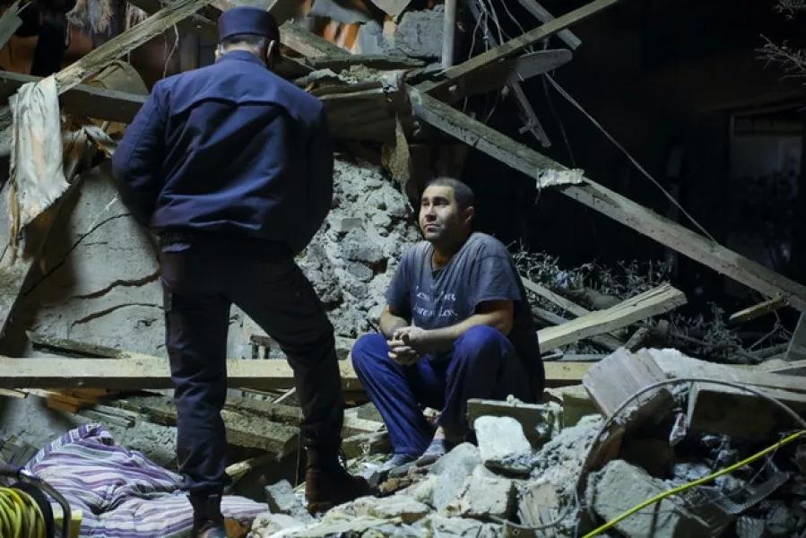 An Azerbaijan’s policeman, left, speaks to a man sitting at his destroyed house in a residential area that was hit by rocket fire overnight by Armenian forces (AP)