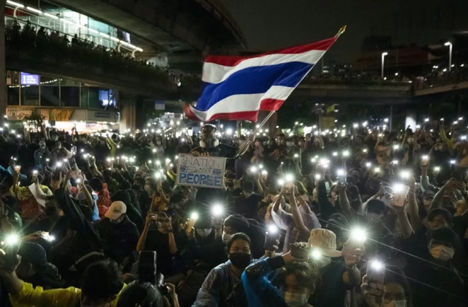 Pro-democracy protesters wave the Thailand national flag as others shine their mobile phone lights during an anti-government protest in Bangkok (Sakchai Lalit/AP)