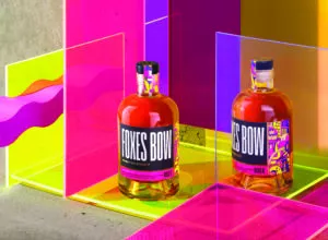 Two bottles of foxes bow whiskey against pink, yellow and purple screens highlighting the colourful design on the bottles