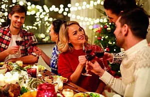 happy friends having christmas dinner at home, drinking red wine and clinking glasses