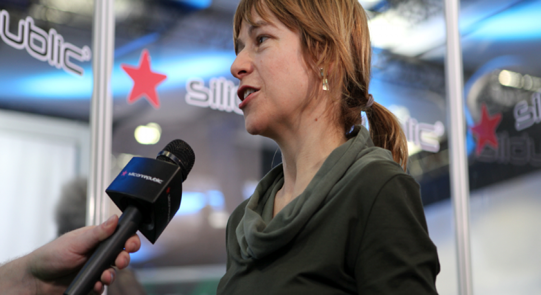 Woman with reddish blonde hair answering questions into a microphone.