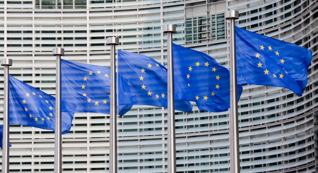 A line of five European flags flying in the wind outside the European Parliament in Brussels.