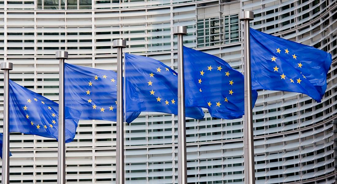 A line of five European flags flying in the wind outside the European Parliament in Brussels.