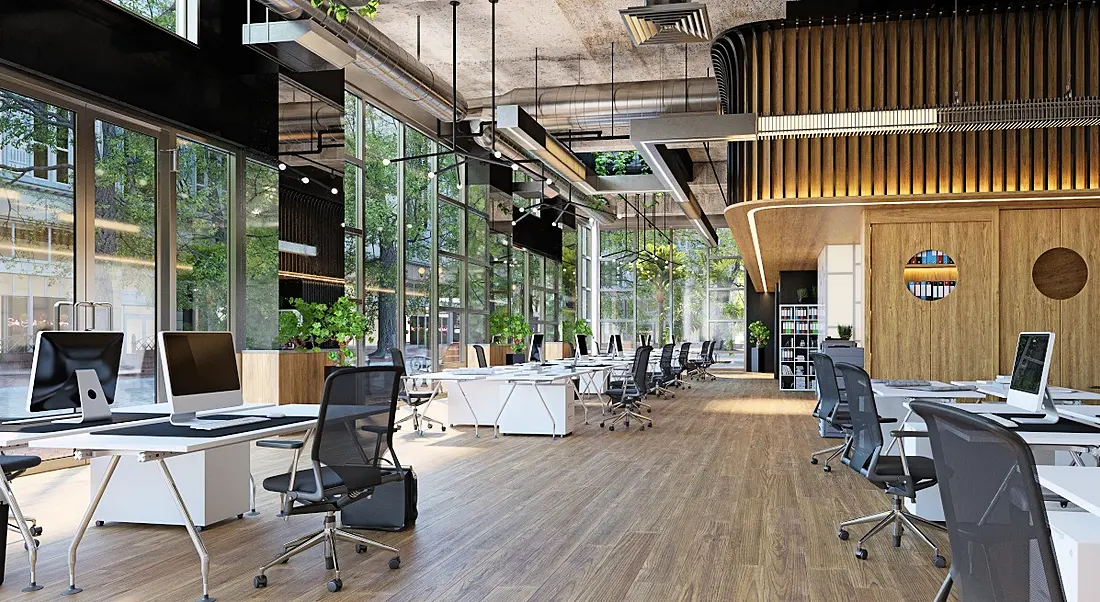 The interior of a modern office, with large glass windows, wooden floors and white desks.