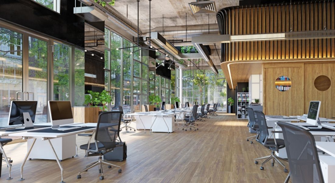 The interior of a modern office, with large glass windows, wooden floors and white desks.