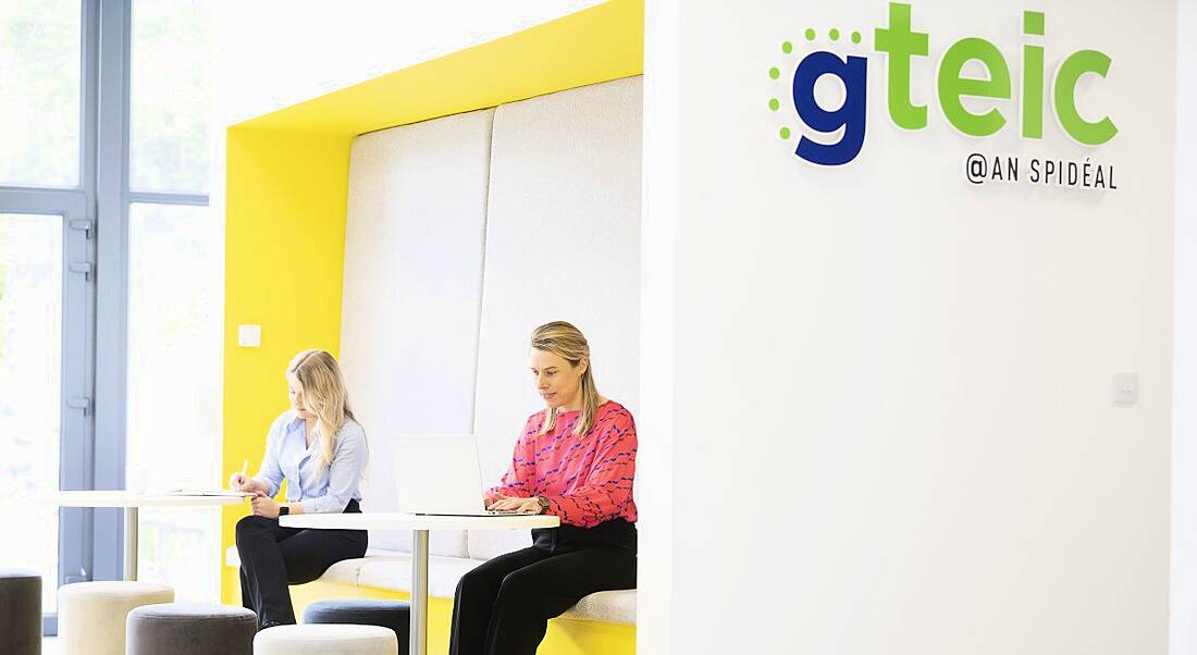 Two women working in digital hub with a 'Gteic' sign on the wall above them.