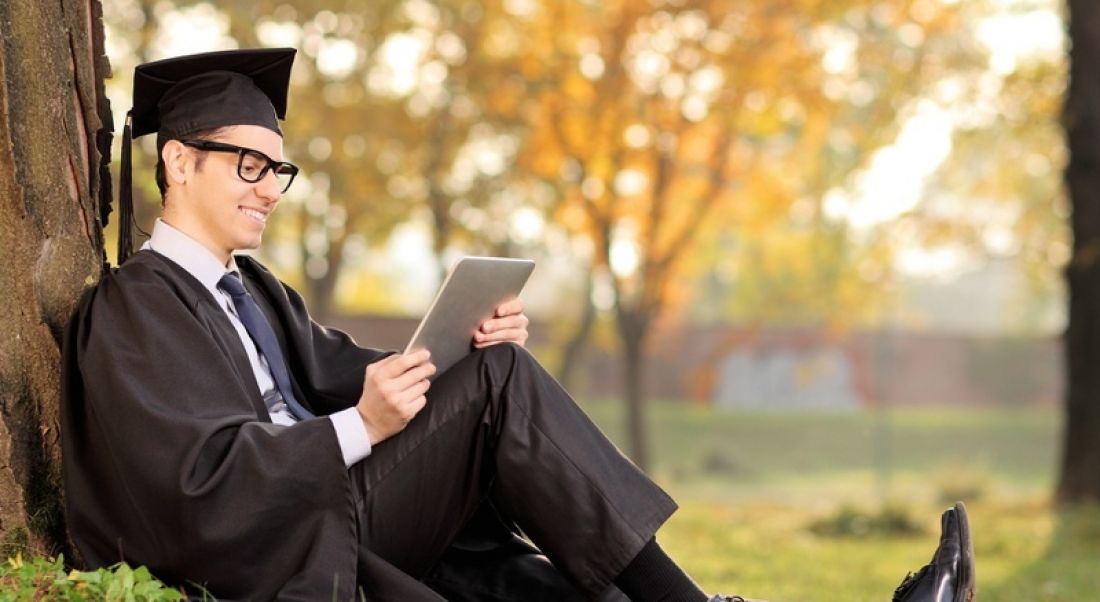 Graduate sitting under tree, using iPad