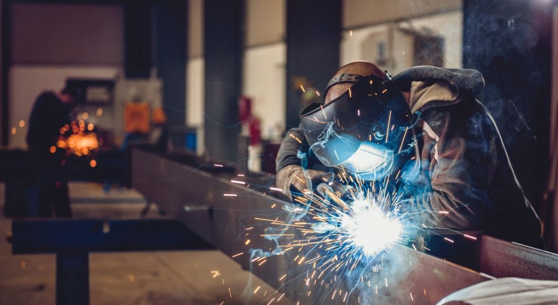 Industrial welder with torch and protective helmet in big hall.