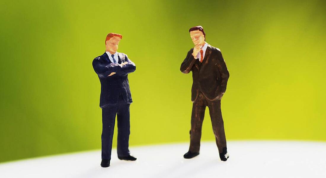 Two figurines in business suits with arms crossed looking confrontational against a lime green background.