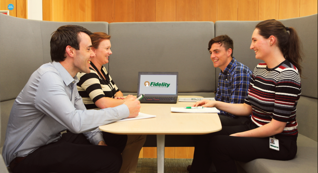 A group of employees meet together in a booth with a laptop between them, its display showing the Fidelity Investments logo.