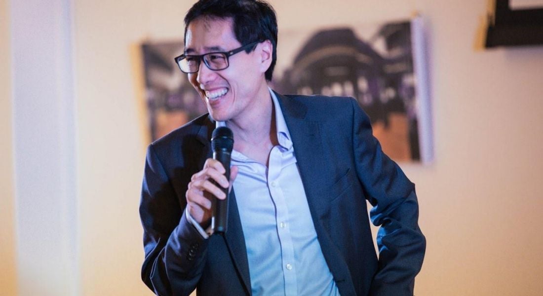 Huy Nguyen Trieu wearing a shirt and blazer speaks into a handheld microphone.