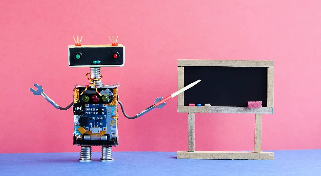 A toy robot pointing to a blackboard teaching you about AI.