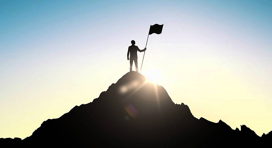 Person at the top of a mountain planting a flag. Depicts success despite having a bad leader.