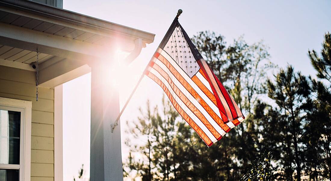 Front side of typical american porch colonial house with American flag out front. H-1B Visa Concerns