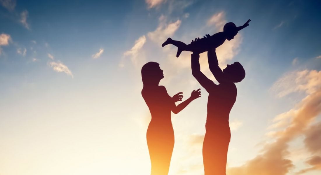 Silhouette of parents on parental leave holding their child happily in the air against a sunset