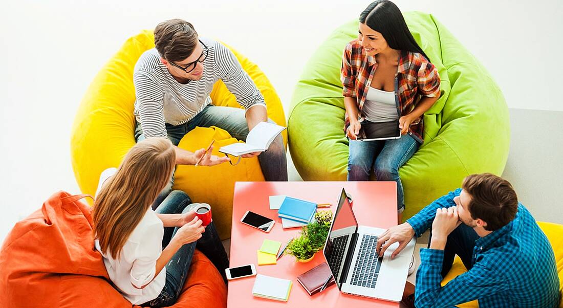 Top view of four young people working together, successfully using productivity tips while sitting at the colourful bean bags