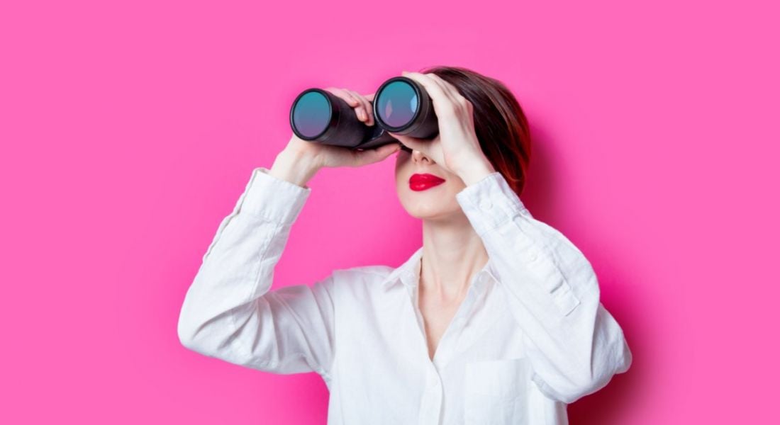 Woman against a pink background holding binoculars, searching for blockchain engineers