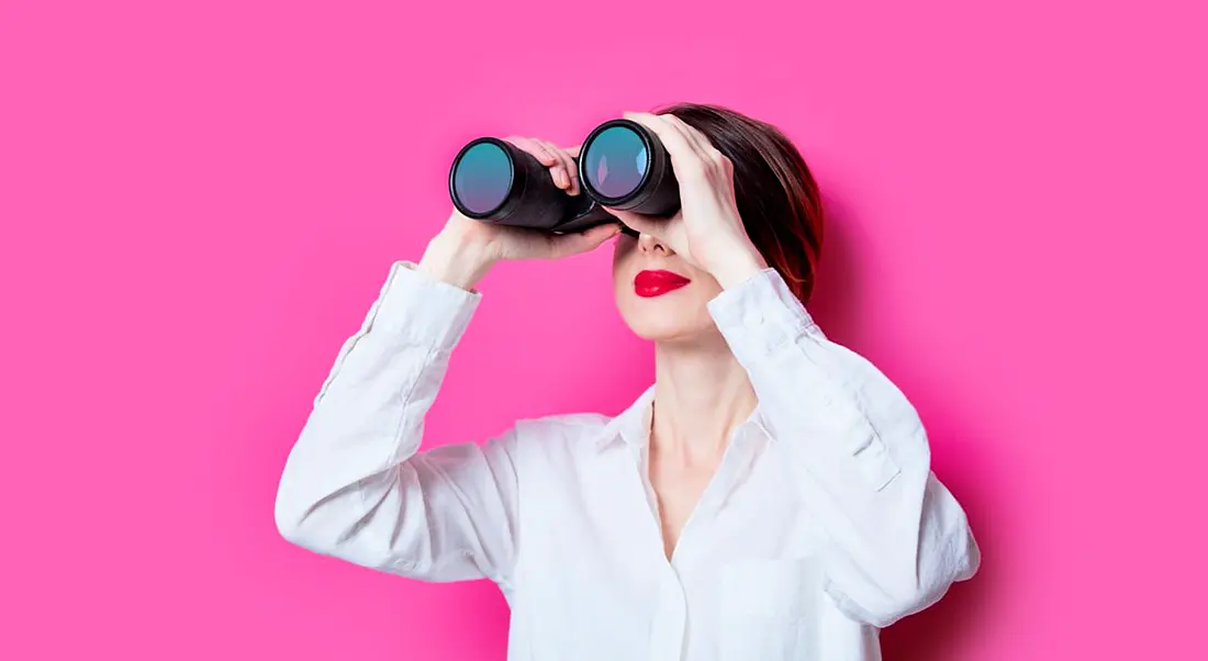 Woman against a pink background holding binoculars, searching for blockchain engineers