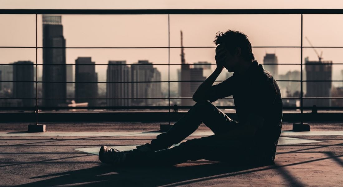 silhouette of man suffering mental health issues sitting on a rooftop overlooking a metropolitan skyline