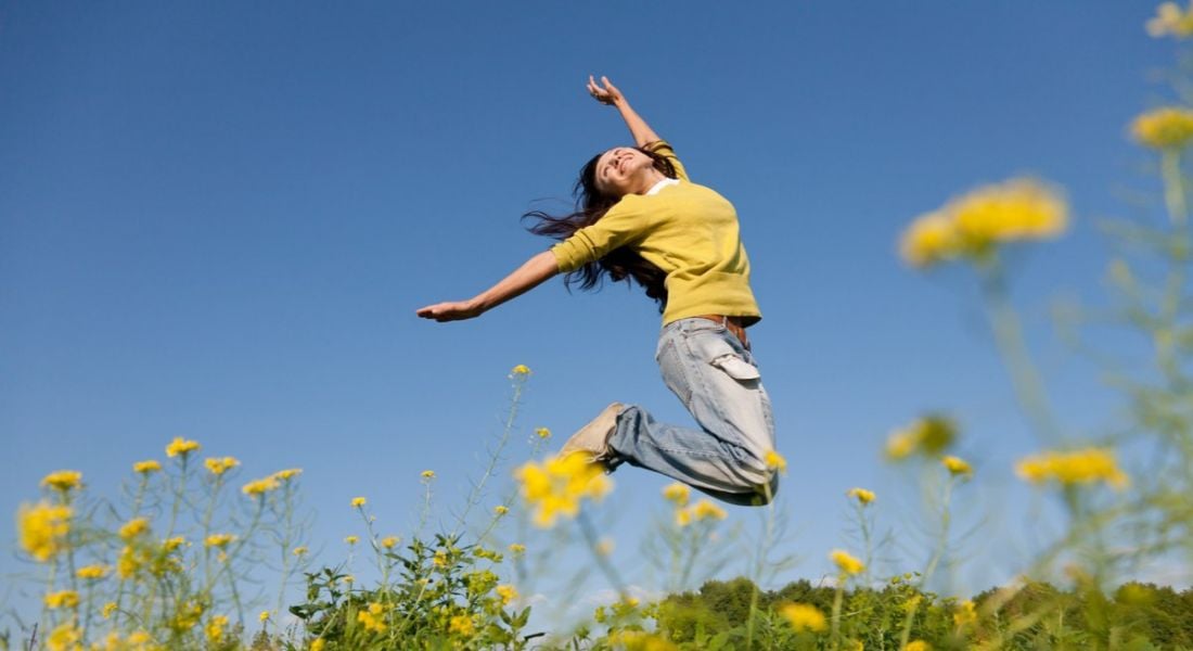 Woman jumping for joy in a ragweed-dotted field on a clear sunny day because of all the jobs that were created in Ireland this week
