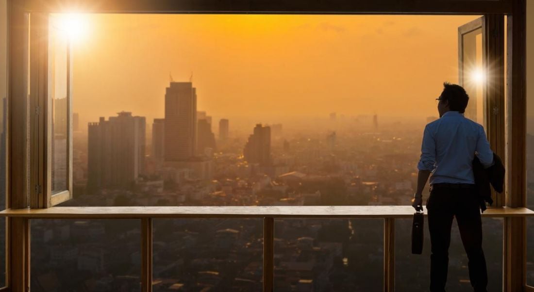 Young business man looking out window at sunrise in metropolitan area. Looking ahead at trends.