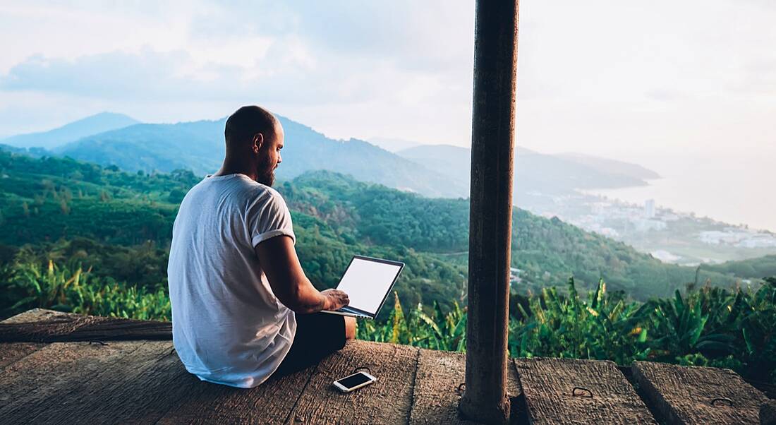 Man on laptop overlooking picturesque mountain range, remote working