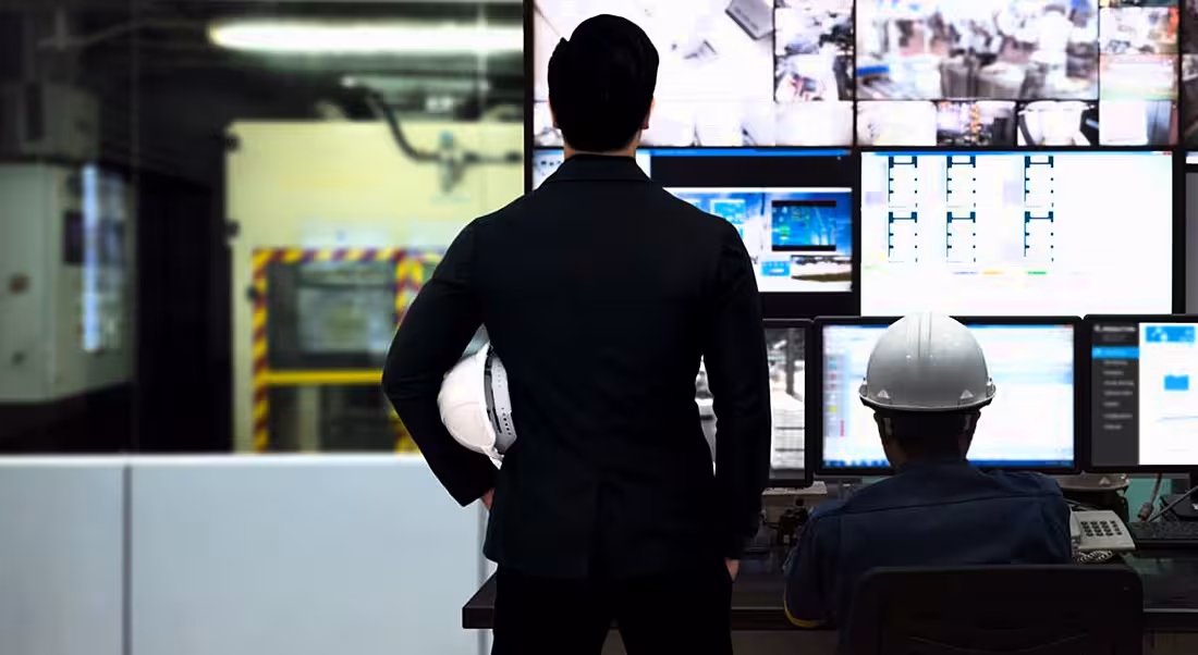 Process control room and industrial automation. One man sitting one man standing looking at array of screens. Robotics automation