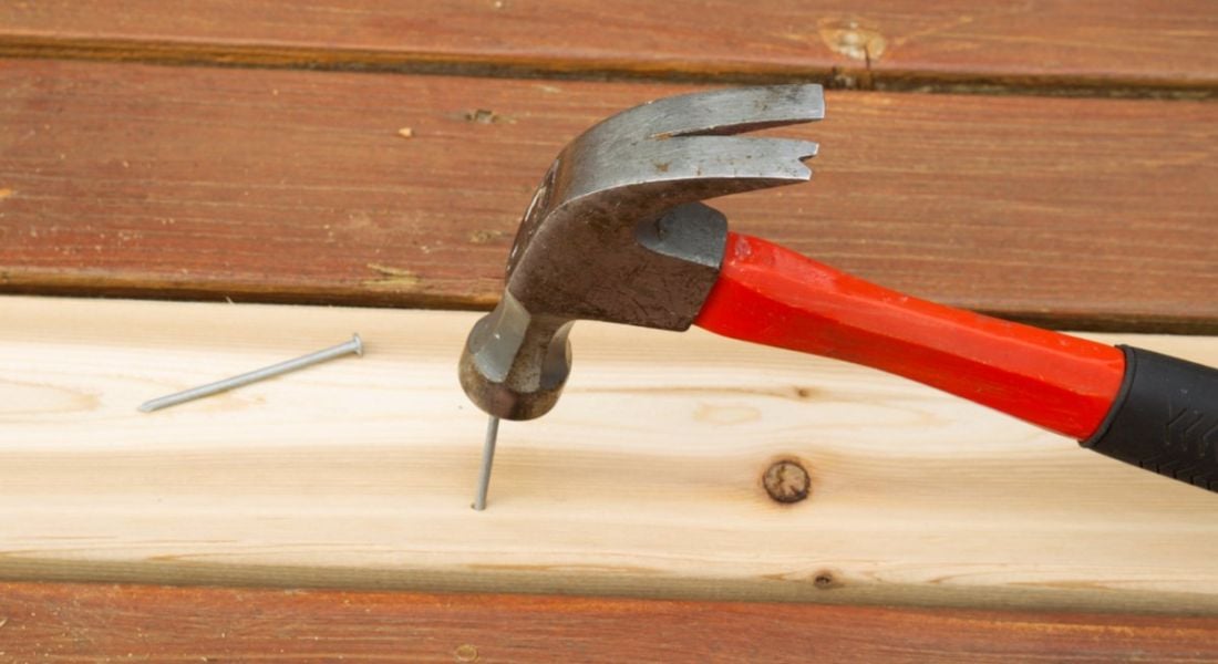 A red hammer hammering a nail into a piece of wood to represent nailing your first performance review.