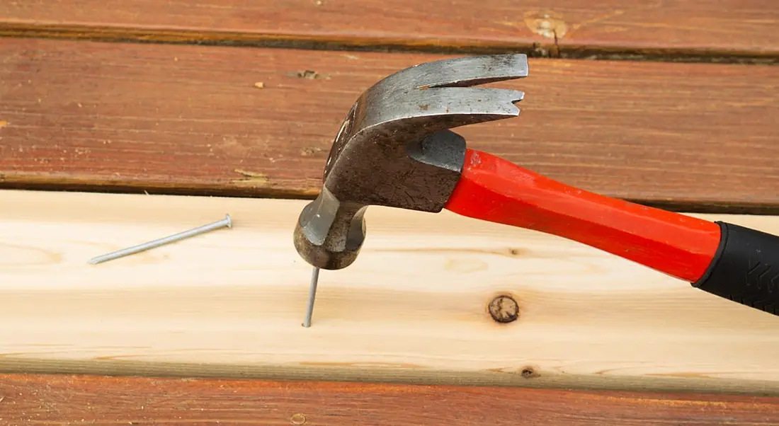 A red hammer hammering a nail into a piece of wood to represent nailing your first performance review.