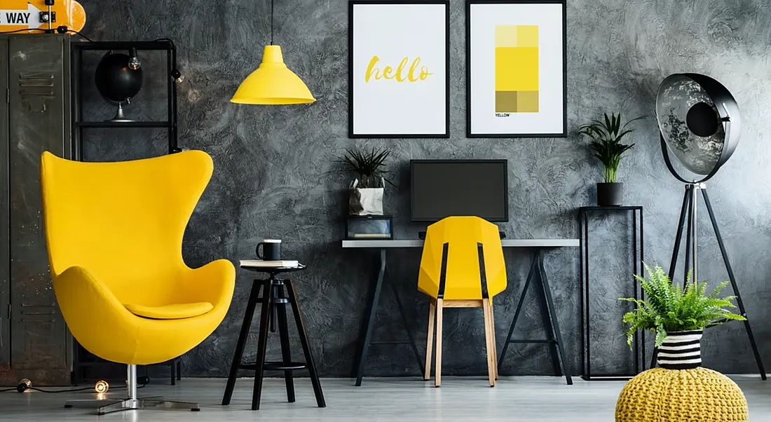 Cool charcoal grey office space with canary yellow arm chair at the left, yellow desk chair and yellow pictures on the wall.