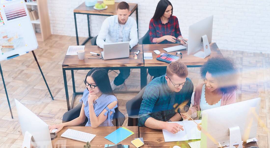 A group of five diverse, young employees working at chic, wooden desks, showing what a cool sci-tech job might look like.