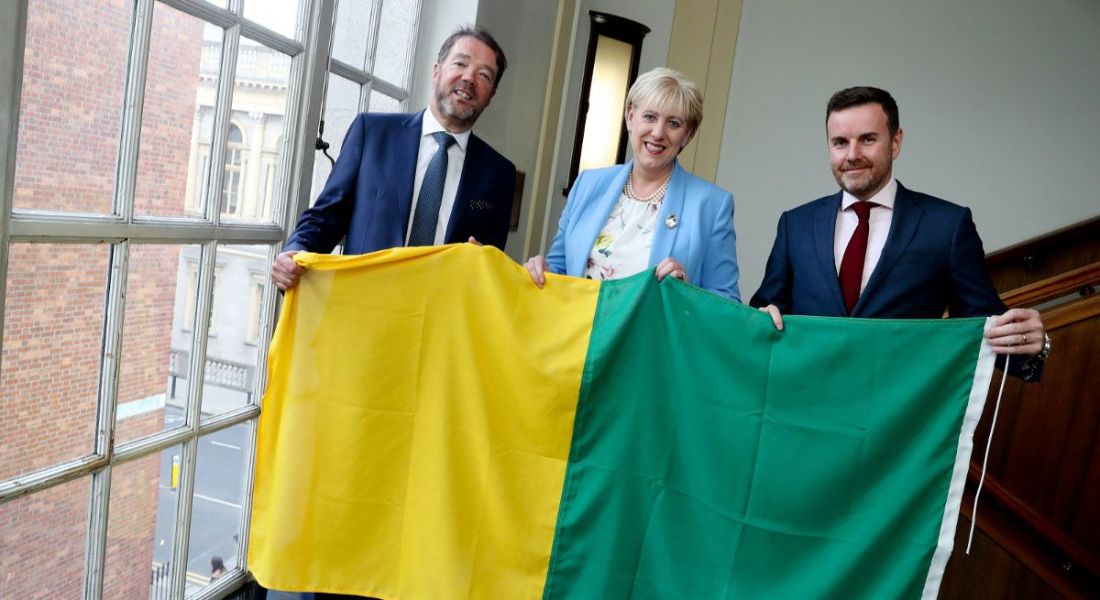 Three people holding the Kerry GAA flag.