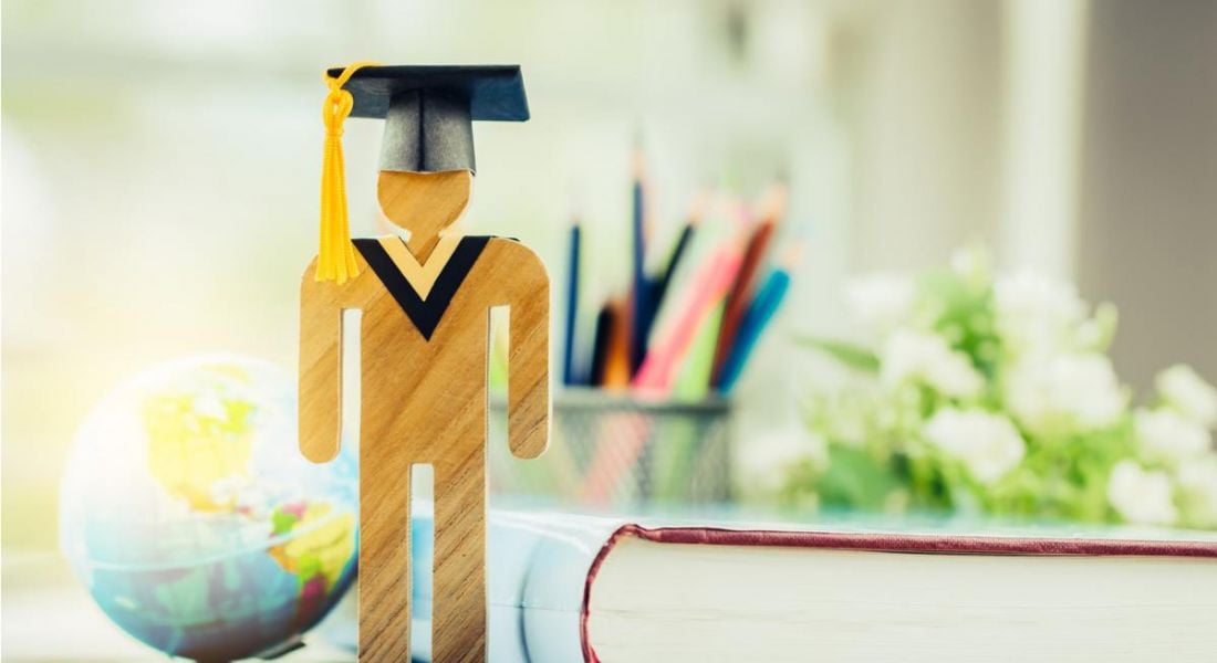 A wooden figurine with a graduation cap on in front of a book, some stationary and a globe wondering about what jobs for graduates exist