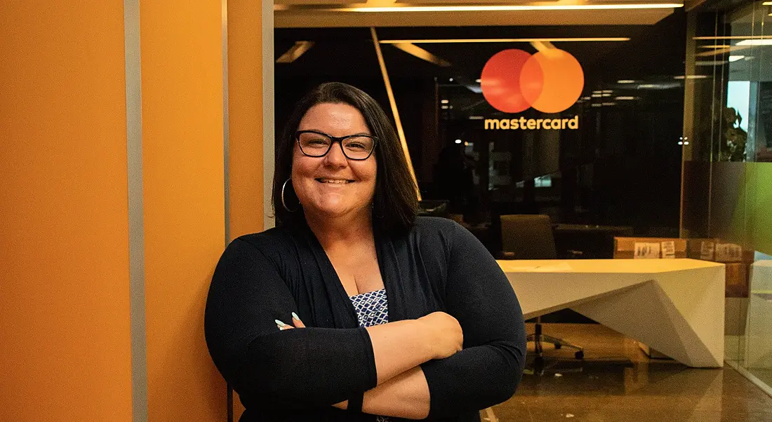 Tammy Hawkins, a smiling brunette woman with glasses standing in the Mastercard offices.