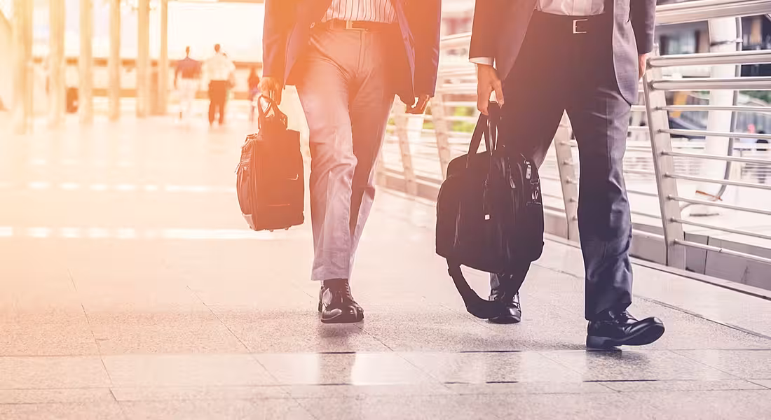 The bottom half of two men in dark-coloured suits and holding briefcases walking side by side.