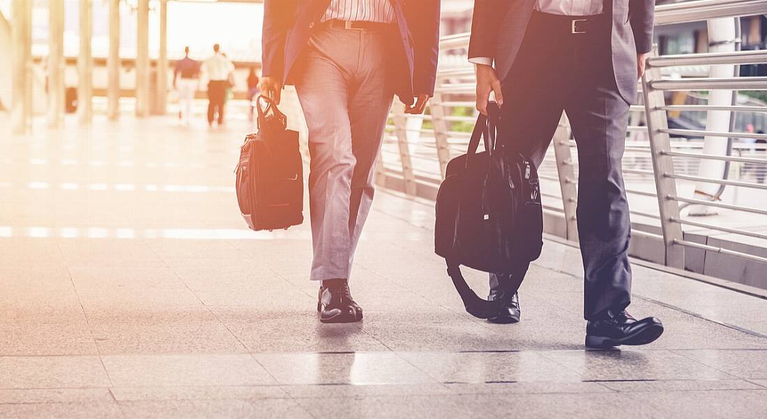 The bottom half of two men in dark-coloured suits and holding briefcases walking side by side.