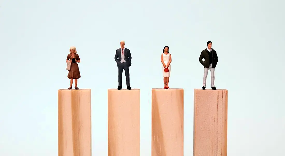 Four small figurines of women and men stand atop wooden platforms of equal height