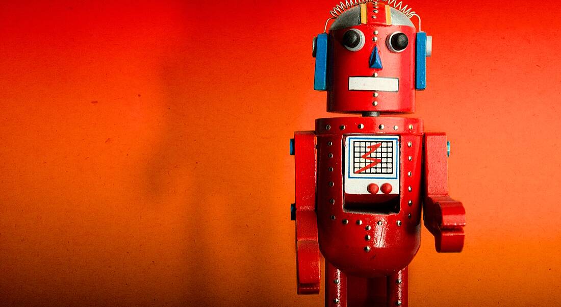 A red toy robot facing the camera. It is standing against an orange-red background.