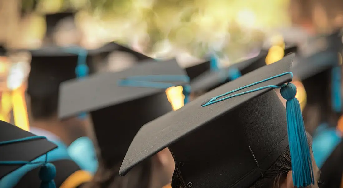 A gaggle of graduations wearing graduation caps with aquamarine tassles. You can only see the tops of their caps.