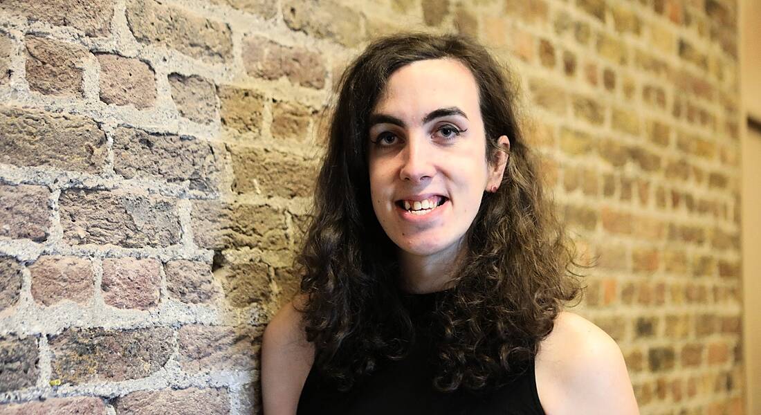 A curly-haired woman in a sleeveless black top smiles next to a brick wall.