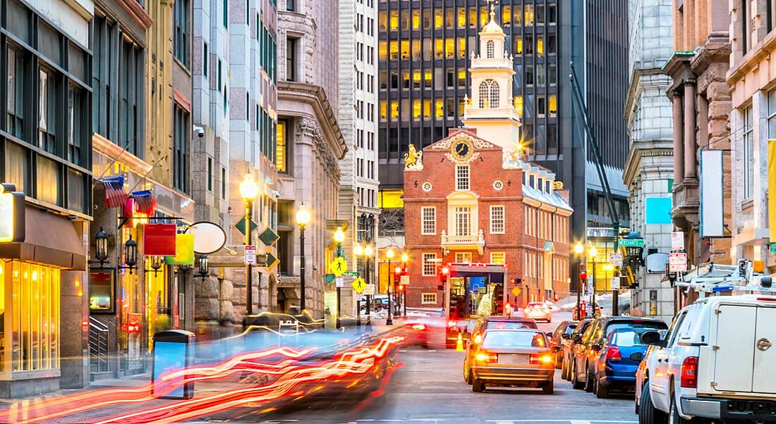 Busy financial district in Boston. Blurry lights of fast cars on a busy road surrounded by tall buildings.