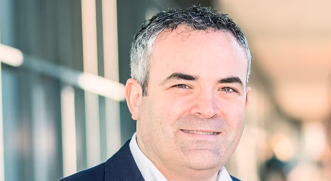 A close headshot of a man with greying hair and slight stubble. He’s a future of work expert, smiling and wearing a suit.