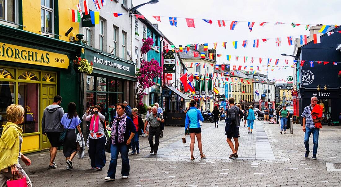 A busy pedestrian street in Galway – where Wayfair is – with bright shopfronts and international flags hanging at the top.