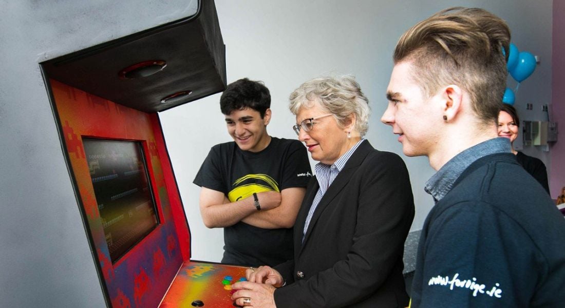 A woman and two teenage boys play on an arcade games console.