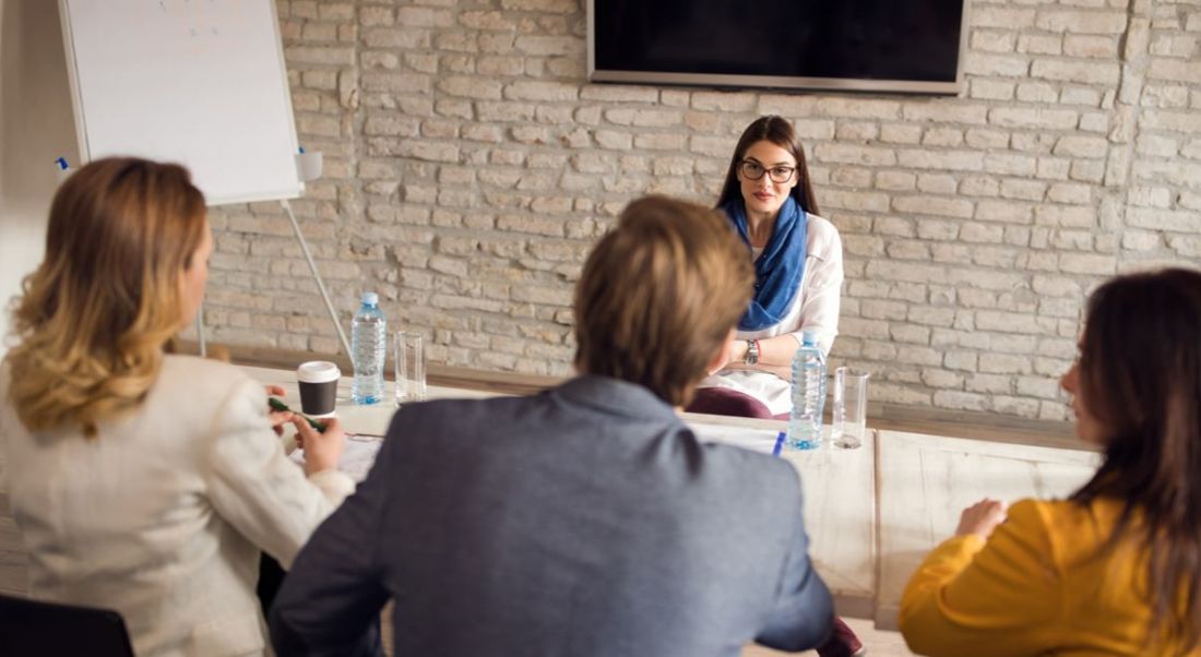 Young woman sitting facing three interviewers – two women and a man. She’s smiling because she got some great interview tips.